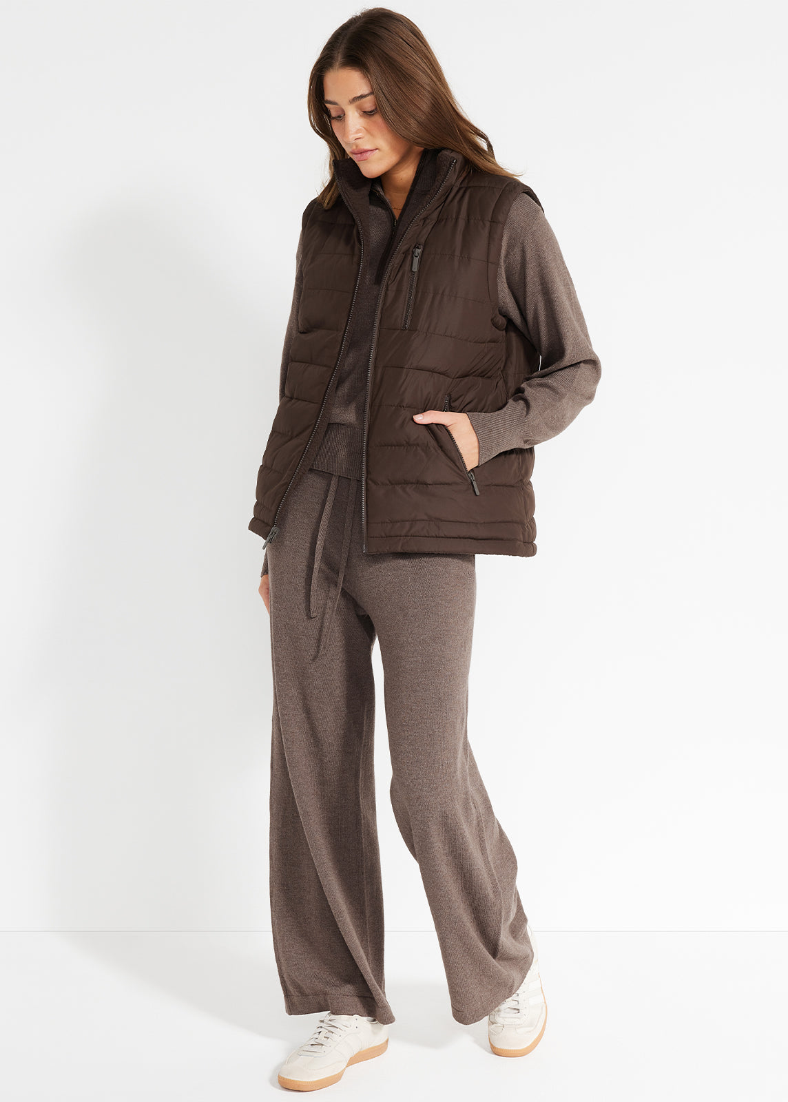 Model wearing brown knit lounge set layered with a puffer vest and white sneakers.